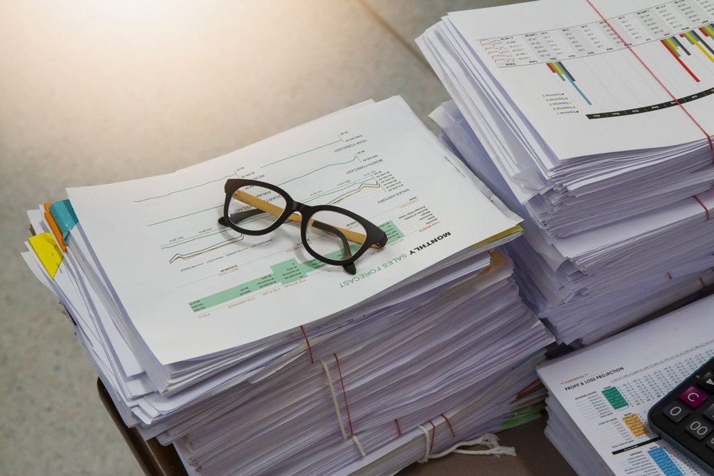 Eyeglasses atop stacked papers with colorful tabs and graphs.